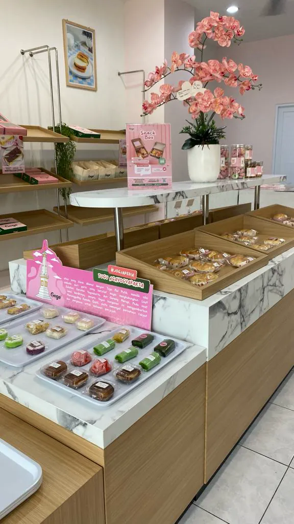 Jajan pasar dalam kemasan di atas meja display dan rak kayu Gege Bakery